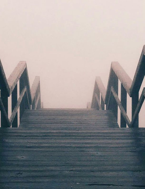 Der Weg geradeaus führt über eine hölzerne, steil ansteigende Bogenbrücke, doch das Ziel liegt im Nebel.