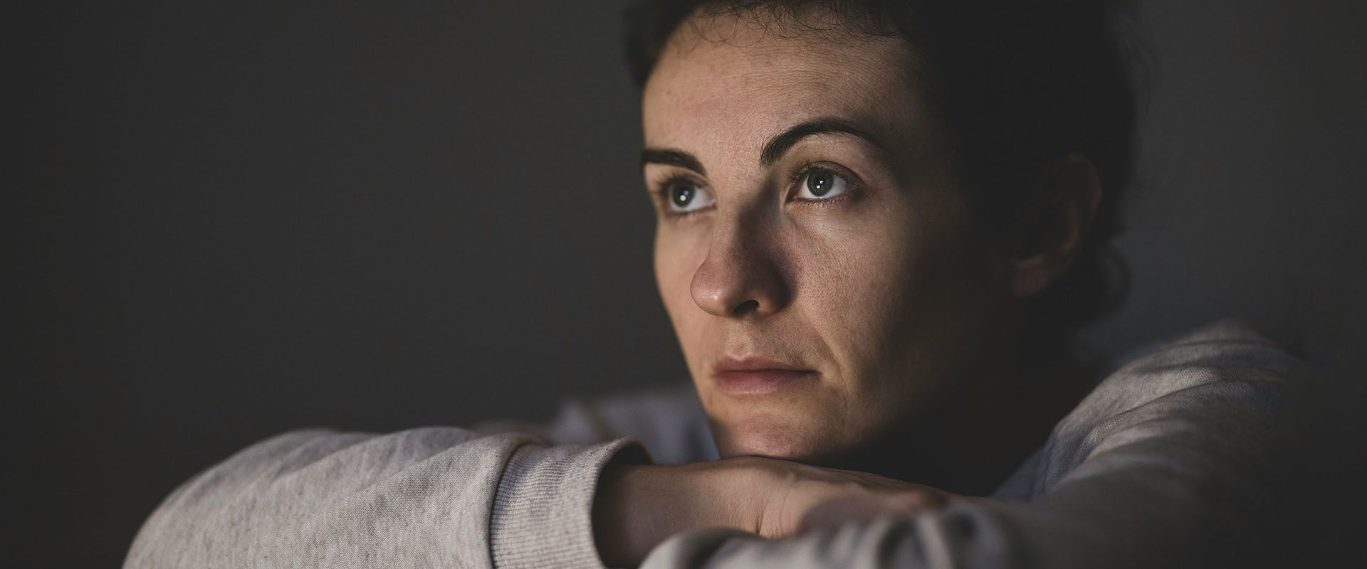 Vor dunklem Hintergrund blickt eine Frau müde in die Ferne.