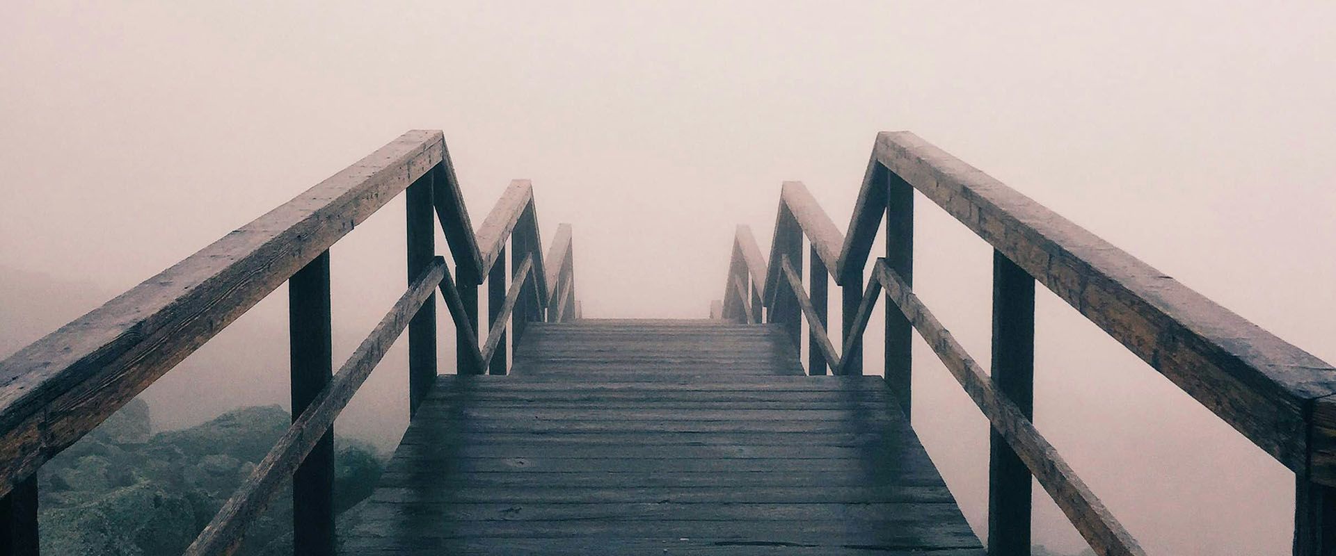 Der Weg geradeaus führt über eine hölzerne, steil ansteigende Bogenbrücke, doch das Ziel liegt im Nebel.